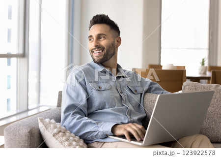 Happy handsome man sitting on couch with laptop Happy handsome man sitting on couch with laptop 123922578