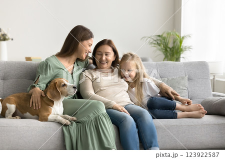 Three generations of women sit close on sofa with dog Three generations of women sit close on sofa with dog 123922587