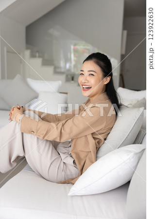 Happy cheerful young Vietnamese homeowner woman resting on comfortable sofa Happy cheerful young Vietnamese homeowner woman resting on comfortable sofa 123922630