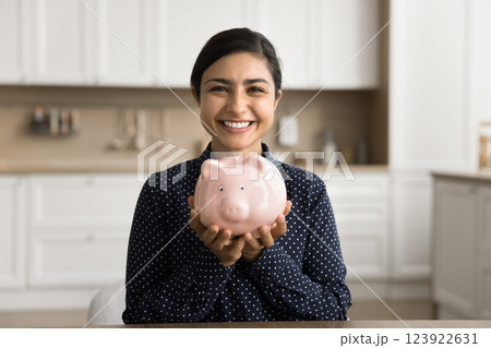 Happy smiling young woman sit at desk show you piggybank 123922631