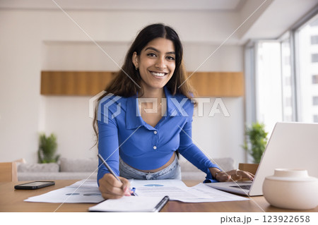 Indian woman working leaning over desk with papers and laptop Indian woman working leaning over desk with papers and laptop 123922658