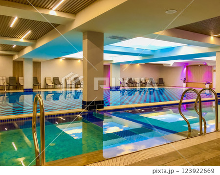 Swimming pool and relaxation area in modern spa center. Indoor swimming pool with lounge chairs and modern lighting. Relaxing spa atmosphere with blue water reflections and stylish bright interior Swimming pool and relaxation area in modern spa center. Indoor swimming pool with lounge chairs and modern lighting. Relaxing spa atmosphere with blue water reflections and stylish bright interior 123922669