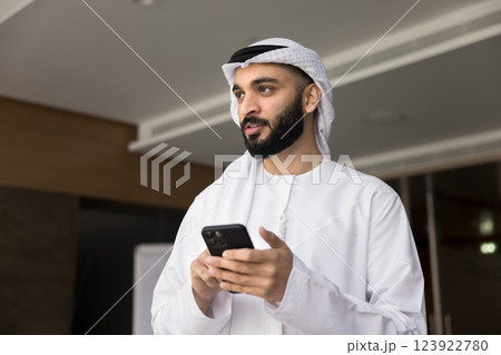 Young man dressed in traditional Middle Eastern dishdasha holding smartphone Young man dressed in traditional Middle Eastern dishdasha holding smartphone 123922780