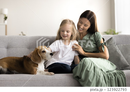 Little girl her mother sits on sofa, gently petting dog Little girl her mother sits on sofa, gently petting dog 123922793