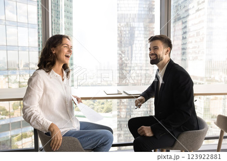 Two young teammates laughing seated at table in modern office 123922881