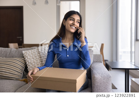 Woman sits on sofa with parcel and talking on smartphone Woman sits on sofa with parcel and talking on smartphone 123922891