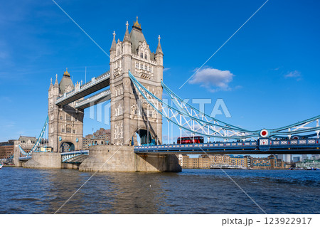 On a bright sunny day in London, Tower Bridge stands majestically over the River Thames. The iconic structure captures the essence of British architecture while a red bus crosses above. 123922917