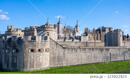 Tower of London stands proudly along the River Thames, showcasing its medieval structure and rich history. Visitors admire its impressive walls and iconic towers under a clear blue sky. 123922923