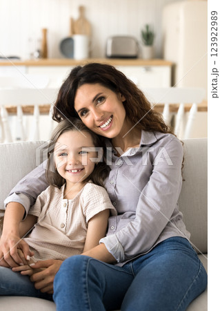 Millennial mom small daughter looking at camera embracing on couch Millennial mom small daughter looking at camera embracing on couch 123922989