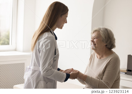 Compassionate young female doctor holding hands of elderly patient grandma Compassionate young female doctor holding hands of elderly patient grandma 123923114