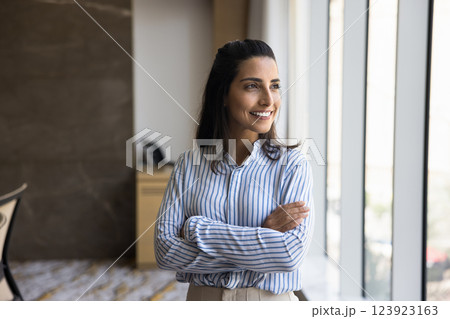 Happy successful Brazilian businesswoman standing in workplace looking out window 123923163