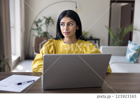 Focused Indian woman working on laptop seated at desk 123923165