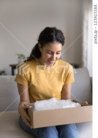 Happy Brazilian young 20s woman sitting on sofa with box Happy Brazilian young 20s woman sitting on sofa with box 123923168
