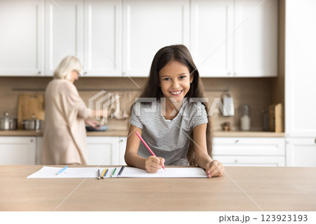 Smiling tween girl drawing while aged grandma cooking at kitchen Smiling tween girl drawing while aged grandma cooking at kitchen 123923193