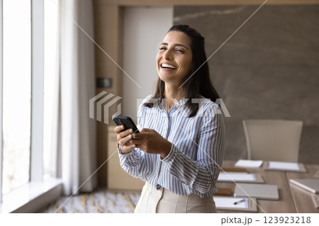 Laughing Brazilian businesswoman holding smartphone standing in meeting room Laughing Brazilian businesswoman holding smartphone standing in meeting room 123923218