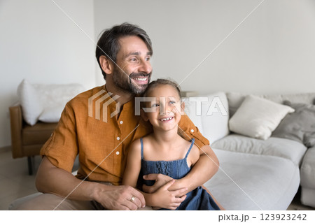 Calm man cuddling little daughter seated together on comfortable sofa Calm man cuddling little daughter seated together on comfortable sofa 123923242