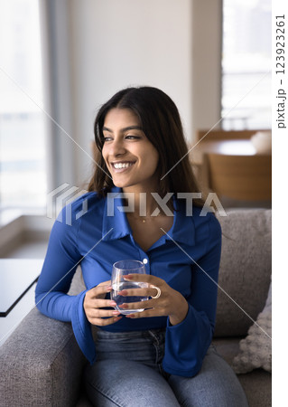 Indian woman sits on couch with glass of natural water Indian woman sits on couch with glass of natural water 123923261