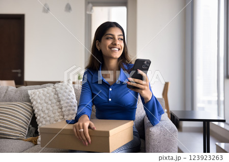Indian woman sits on sofa with box and smartphone 123923263