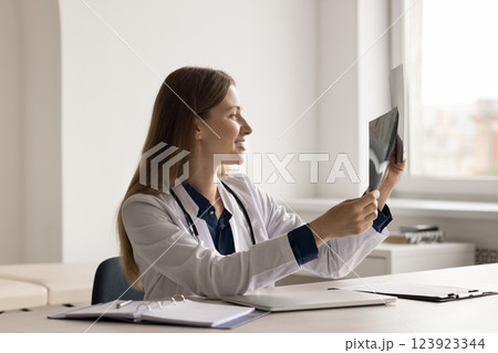 Smiling millennial woman doctor reading radiological images at work desk Smiling millennial woman doctor reading radiological images at work desk 123923344