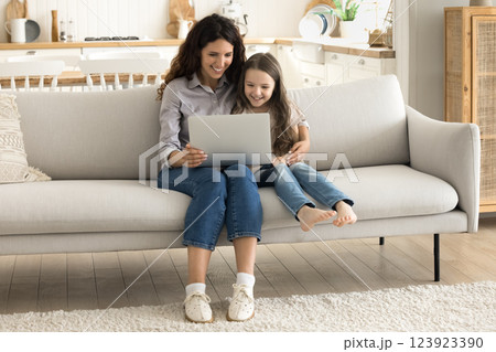 Millennial mother sitting on couch with little daughter using notebook 123923390