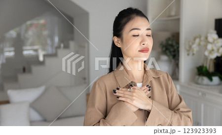 Calm peaceful young Asian woman keeping hands on chest 123923393