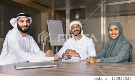 Three professionals sit together at conference table, smiling at camera 123923523