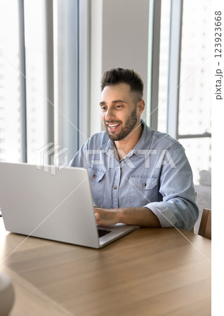 Smiling man sitting at desk working on studying using laptop 123923668