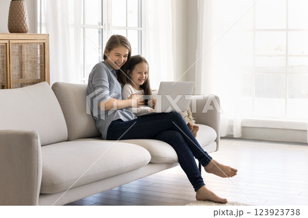 Friendly young mom little daughter using notebook in living room Friendly young mom little daughter using notebook in living room 123923738