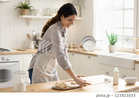 Smiling young woman rolling dough on kitchen table preparing pies 123923833