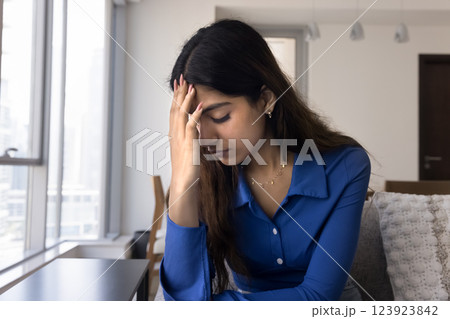 Young Indian woman sit on sofa looks stressed and worried Young Indian woman sit on sofa looks stressed and worried 123923842
