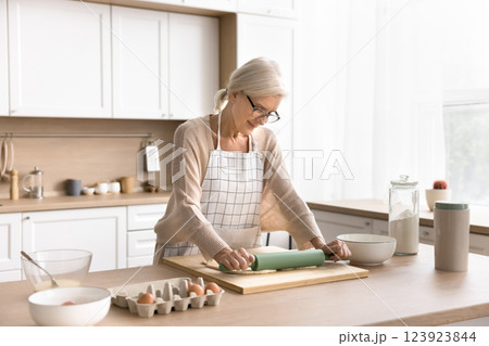 Inspired middle aged housewife in apron roll dough at kitchen Inspired middle aged housewife in apron roll dough at kitchen 123923844