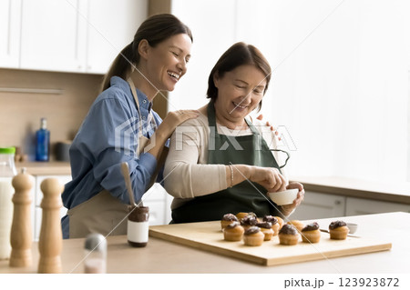 Older woman placing sprinkles on cupcakes while daughter hugging her 123923872