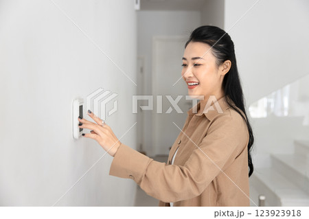 Happy young Asian homeowner woman typing on climate control panel, Happy young Asian homeowner woman typing on climate control panel, 123923918