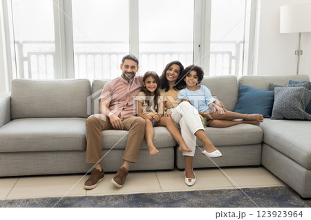 Happy family sitting together on sofa, smiling, looking at camera Happy family sitting together on sofa, smiling, looking at camera 123923964