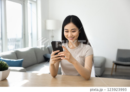Pretty Asian woman sitting at table holding her phone 123923993