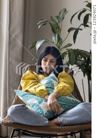 Sad woman hugging pillow while sitting curled up in chair Sad woman hugging pillow while sitting curled up in chair 123924071