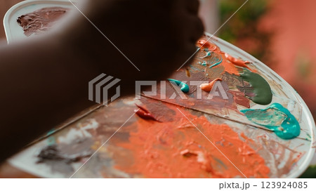 Talented artist using modern tools and painting supplies to create an artwork, mixing watercolors on a palette during his creative process. Man working on a masterpiece. Close up. Camera A. 123924085
