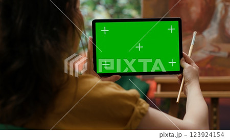 Female artist holding device with green screen in art and craft atelier, admiring rustic artwork painted with watercolor paint. Woman preparing a masterpiece for an art gallery exhibition. Camera A. 123924154