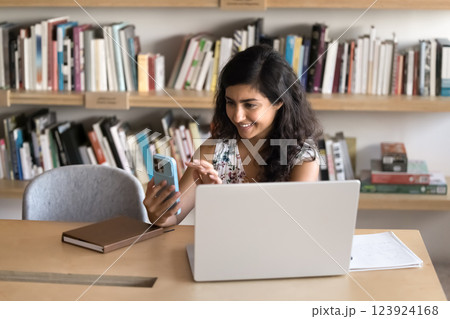 Happy female student make videocall distracted from notebook at library Happy female student make videocall distracted from notebook at library 123924168