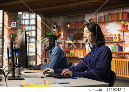 Team of customer service staff members tracking support ticket in dedicated company software on PC. Asian call center worker and african american colleague talking with customer calling 123924242