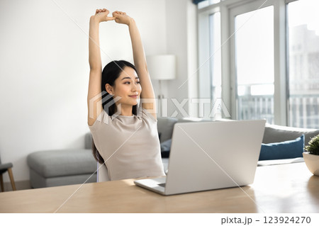 Woman take break, stretching arms seated at desk with laptop Woman take break, stretching arms seated at desk with laptop 123924270