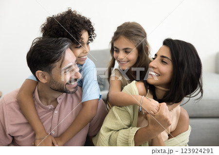 Parents and playful children embracing each other seated on couch 123924291