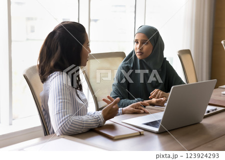 Multicultural businesswomen having conversation seated at table with laptop Multicultural businesswomen having conversation seated at table with laptop 123924293