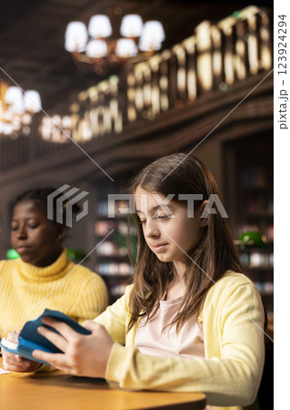 Young teenagers reading literary texts at the library as part of their curriculum, preparing for literature class lesson and enhancing their academic focus. Girls read the mandatory books titles. 123924294