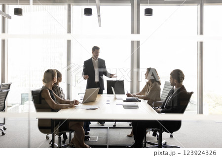 Stakeholders sit at conference table listening speech of businessman standing 123924326