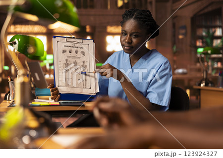 Black med school students team reading anatomy textbooks and thesis notes at the library, learning session for a successful career. Pupils focusing on exam preparation for their diploma. Black med school students team reading anatomy textbooks and thesis notes at the library, learning session for a successful career. Pupils focusing on exam preparation for their diploma. 123924327