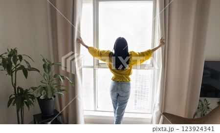 Rearview woman standing in front of window and opening curtains Rearview woman standing in front of window and opening curtains 123924341
