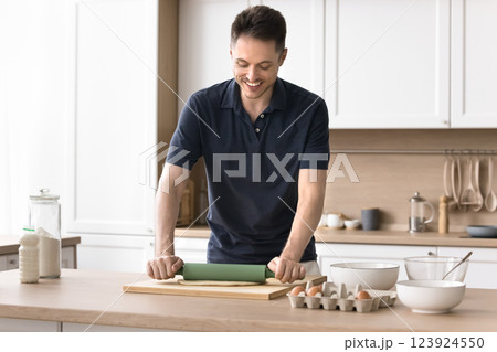 Smiling millennial male enjoy cooking at home kitchen roll dough 123924550