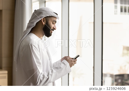 Arabian businessman in white dishdasha using modern smartphone 123924606