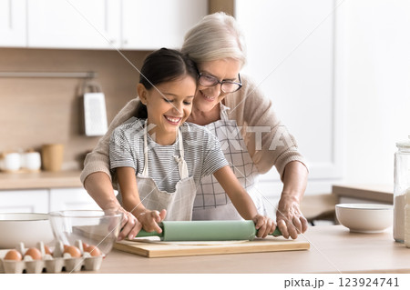 Caring aged grandmother teach little child grandkid to roll dough Caring aged grandmother teach little child grandkid to roll dough 123924741